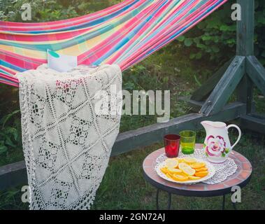 Coin détente dans le jardin. Cadre extérieur en été. Hamac. Tranches d'orange, de verres et de carafe sur une petite table basse. Banque D'Images