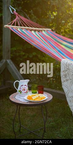 Coin détente dans le jardin. Cadre extérieur en été. Hamac. Tranches d'orange, de verres et de carafe sur une petite table basse. Banque D'Images