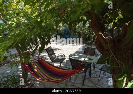 Hamac coloré et zone de loisirs avec le soleil brillant à travers les branches d'arbres verts, temps de loisirs d'été dans la cour traditionnelle grecque de maison avec pierre d Banque D'Images