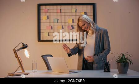 Femme d'affaires enceinte souriante se branle à l'ordinateur portable au bureau Banque D'Images