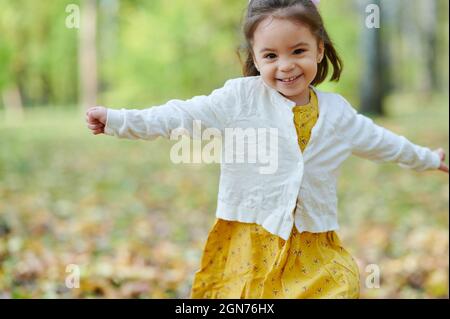 Bonne petite fille courir dans le parc d'automne sur fond flou Banque D'Images