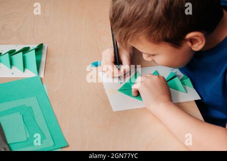 Étape 7 de la création de la carte de Noël. La carte de vœux est presque prête. Décorez-le. Enfant dessine des flocons de neige avec un stylo bleu Banque D'Images