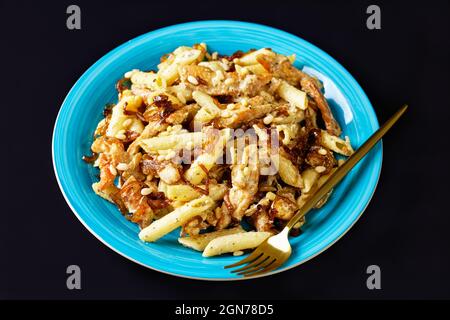 penne de pâtes alfredo de poulet à l'oignon caramélisé arrosé de pignons de pin et de parmesan râpé sur une assiette bleue sur fond noir, horizontale Banque D'Images