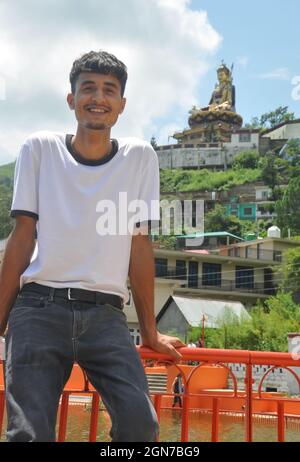Un beau gars souriant assis sur la barrière de sécurité au bord du lac et belle région vallonnée de TSO-Pema et statue de Padmasambhava (Guru Rinpoché) en arrière-plan Banque D'Images