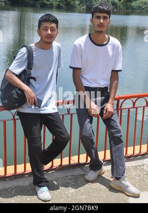 Portrait de deux amis mâles assis sur la barrière de sécurité près du lac et regardant l'appareil photo Banque D'Images