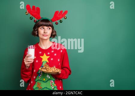 Photo d'adorable femme mignonne vêtue rouge pull-overs bois tenant le lait pain d'épice vide espace isolé couleur vert fond Banque D'Images