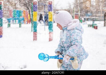 fille avec chute de neige sur le terrain de jeu parmi les maisons en hiver. Jeux de boules de neige actifs dans la rue Banque D'Images