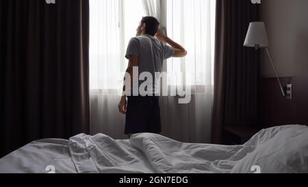 Homme regardant par-dessus la fenêtre dans la chambre. Chambre d'hôtel, inspiration, curiosité, concepts énergétiques du matin Banque D'Images