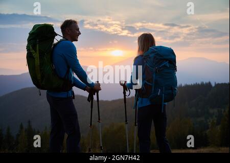 Mari heureux de regarder sa femme qui admirait la vue sur les sommets de montagne et ciel nuageux le soir. Vue arrière couple de randonneurs qui contemplent la vue panoramique de la montagne beskids au coucher du soleil. Banque D'Images