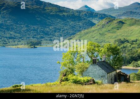 Le long de la West Highland Way en Écosse. Vue sur le Loch Lomond montrant une vieille petite maison blanche cachée derrière des arbres et des buissons Banque D'Images