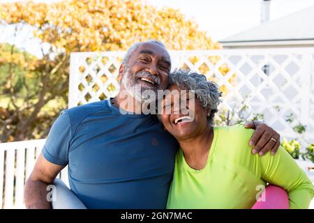 Couple senior afro-américain souriant tenant des tapis de yoga dans le jardin et regardant la caméra Banque D'Images