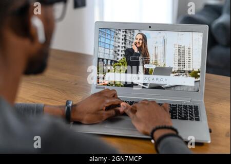 Homme afro-américain utilisant un ordinateur portable pour parcourir les opportunités de travail, chercheur noir sans emploi à la recherche de nouveaux postes vacants sur le site Web, en utilisant l'application informatique pour la recherche d'emploi indépendant. Vue arrière à l'écran Banque D'Images