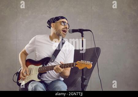 Portrait d'un musicien masculin qui chante une chanson dans un microphone et joue de la guitare électrique. Banque D'Images