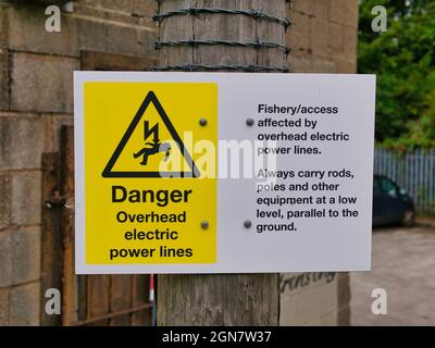 Un panneau de danger jaune et blanc sur le canal Leeds-Liverpool à Lancashire, au Royaume-Uni, avertissant les pêcheurs de lignes électriques aériennes. Banque D'Images