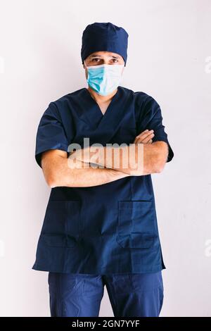 Infirmière, médecin ou vétérinaire de sexe masculin portant un masque bleu et un uniforme bleu foncé à l'hôpital, bras croisés, sourire. Concept de médecine, d'hôpital et de soins de santé. Banque D'Images