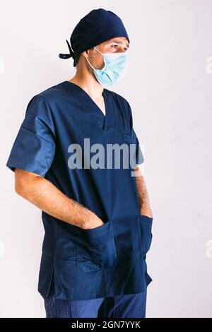 Infirmière, médecin ou vétérinaire de sexe masculin portant un masque bleu et un uniforme bleu foncé à l'hôpital, mains dans les poches, souriant. Concept de médecine, d'hôpital et de soins de santé. Banque D'Images