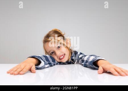 Portrait d'une belle petite fille regardant l'appareil photo, faisant des visages isolés sur fond gris de studio. Émotions humaines, concept d'expression faciale. Banque D'Images