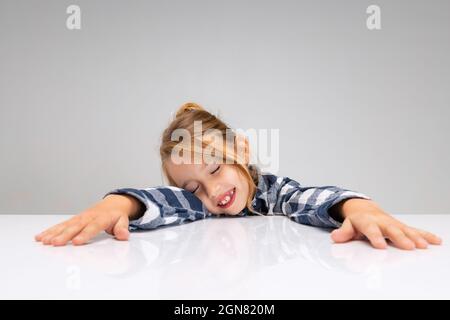 Portrait d'une belle petite fille regardant l'appareil photo, faisant des visages isolés sur fond gris de studio. Émotions humaines, concept d'expression faciale. Banque D'Images