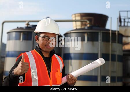 ingénieur debout devant une grande raffinerie de pétrole avec plan sur la main Banque D'Images