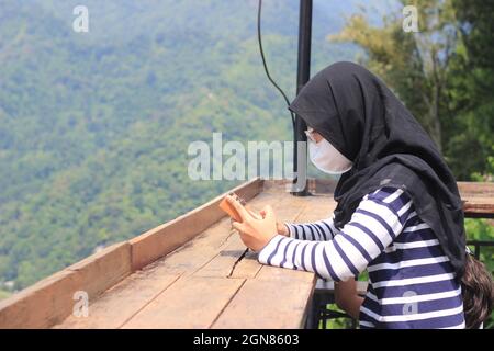 Indonésie Muslimah ou Islam Girl Hold Kalimba, instrument de musique acoustique d'afrique avec la montagne pancar comme fond Banque D'Images