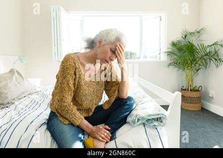 Femme caucasienne âgée fatiguée avec mal de tête assise sur le lit à la maison Banque D'Images