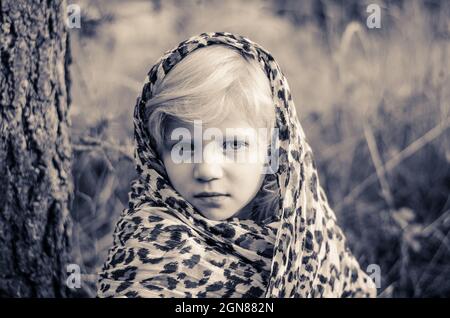 petite fille charmante avec de longs cheveux blonds avec foulard se détendre dans la forêt automnale monochrome Banque D'Images