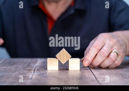 maquette de modèle de trois cubes de bloc de bois , centre un pivoté pour former un diamant avec un homme en arrière-plan Banque D'Images