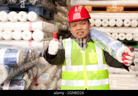 Travailleur d'usine de textile portant le tissu de matière première sur son épaule avec le pouce vers le haut Banque D'Images