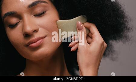 femme afro-américaine utilisant la pierre de gua sha isolée sur gris Banque D'Images