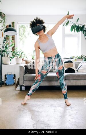 Femme utilisant un micro-casque de réalité virtuelle pendant qu'elle s'exerce dans son salon Banque D'Images