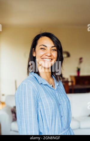 Jeune femme souriante debout à la maison Banque D'Images
