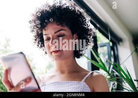 Jeune femme messagerie texte par téléphone intelligent à la maison Banque D'Images