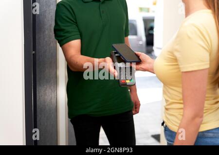 Femme effectuant le paiement sans contact à l'livreur par téléphone mobile à la porte Banque D'Images