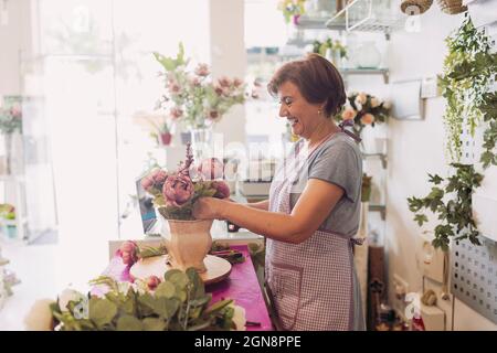 Fleuriste mûr et gai organisant des fleurs tout en étant debout à table dans le magasin Banque D'Images