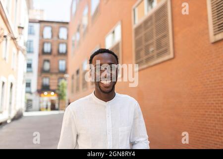 Jeune homme en lunettes souriant devant les bâtiments Banque D'Images