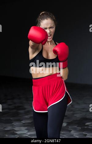 Boxer féminin agressif, en train de poinçonner tout en pratiquant au sous-sol Banque D'Images