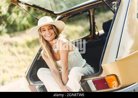 Femme blonde avec chapeau assis dans le coffre de voiture Banque D'Images