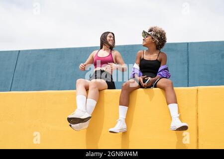 Des amies souriantes assises sur un mur de soutènement jaune Banque D'Images