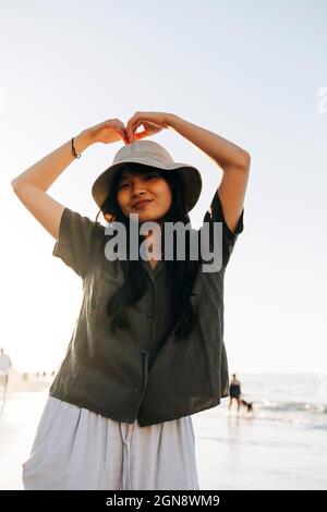 Jeune femme souriante portant un chapeau faisant des gestes à la plage Banque D'Images