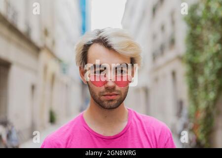 Jeune homme gay portant des lunettes de soleil roses en forme de coeur Banque D'Images