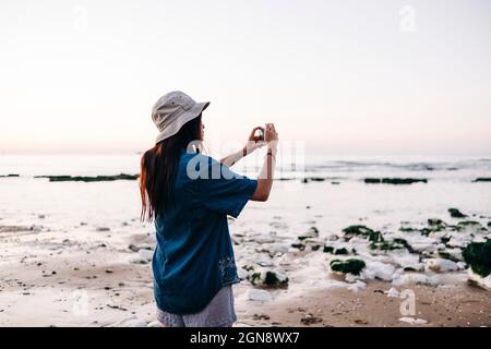 Femme portant un chapeau photographiant à la plage pendant les vacances Banque D'Images