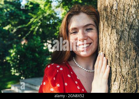 Bonne jeune femme par tronc d'arbre dans le parc Banque D'Images