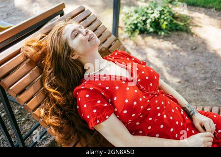Jeune femme en robe rouge allongé sur une chaise longue dans le parc Banque D'Images