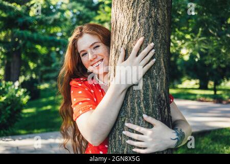 Bonne jeune femme embrassant l'arbre dans le parc Banque D'Images