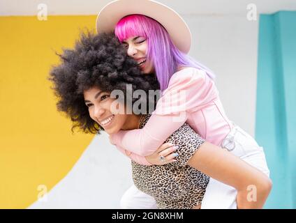 Afro femme coggyendant amie féminine gaie devant le mur Banque D'Images