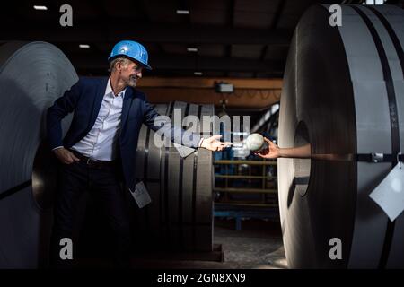 Homme d'affaires senior avec casque hardhat prenant le globe de la main à l'intérieur de la feuille de métal rouleau Banque D'Images