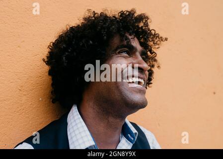 Joyeux jour à l'homme en rêvant tout en s'appuyant sur un mur beige Banque D'Images