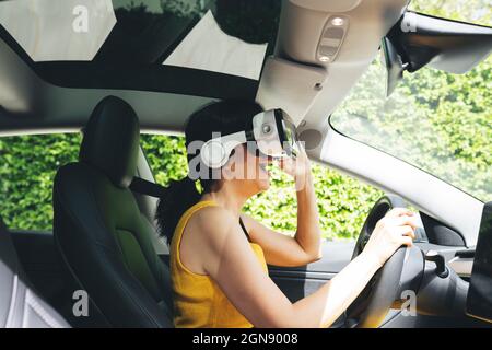 Femme excitée portant un simulateur de réalité virtuelle en conduisant une voiture électrique Banque D'Images