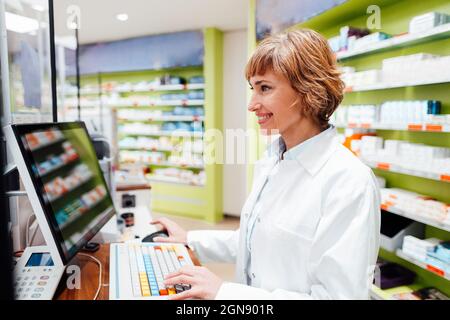 Une femme souriante qui se tient debout dans un magasin médical à l'aide d'un ordinateur Banque D'Images