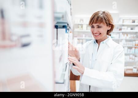 Pharmacien souriant portant un blouse de laboratoire recherchant des médicaments à la pharmacie Banque D'Images